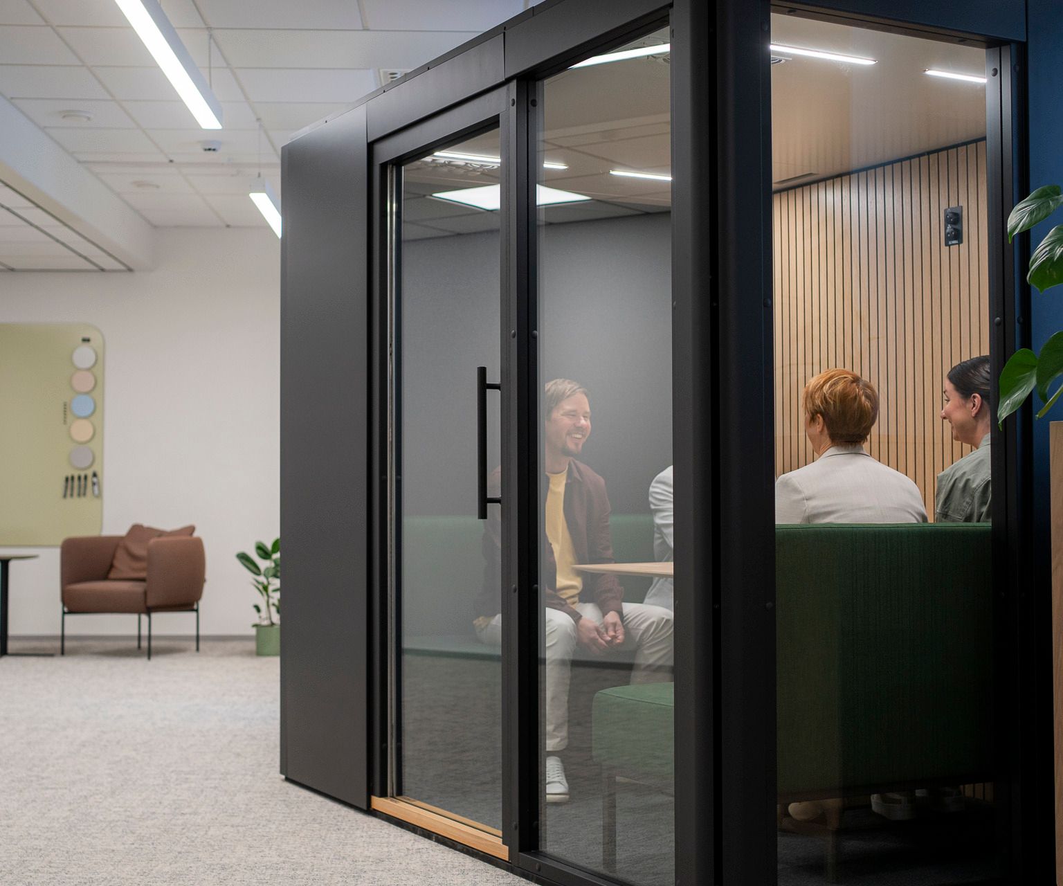 Three office workers sit in an Octacell workroom with glass walls and black outside surfaces