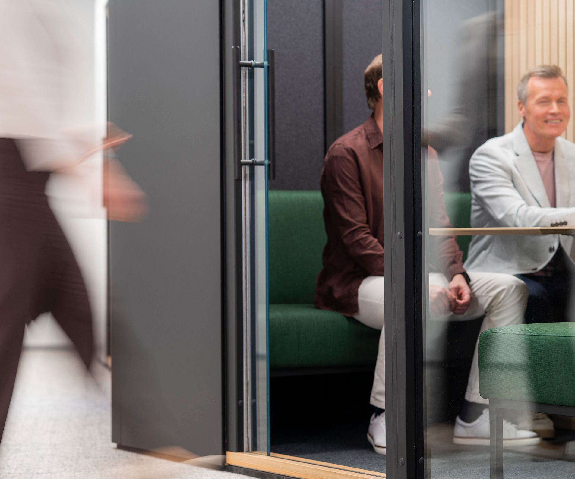 Two men sitting in an Octacell workroom, seen through an open door and glass wall