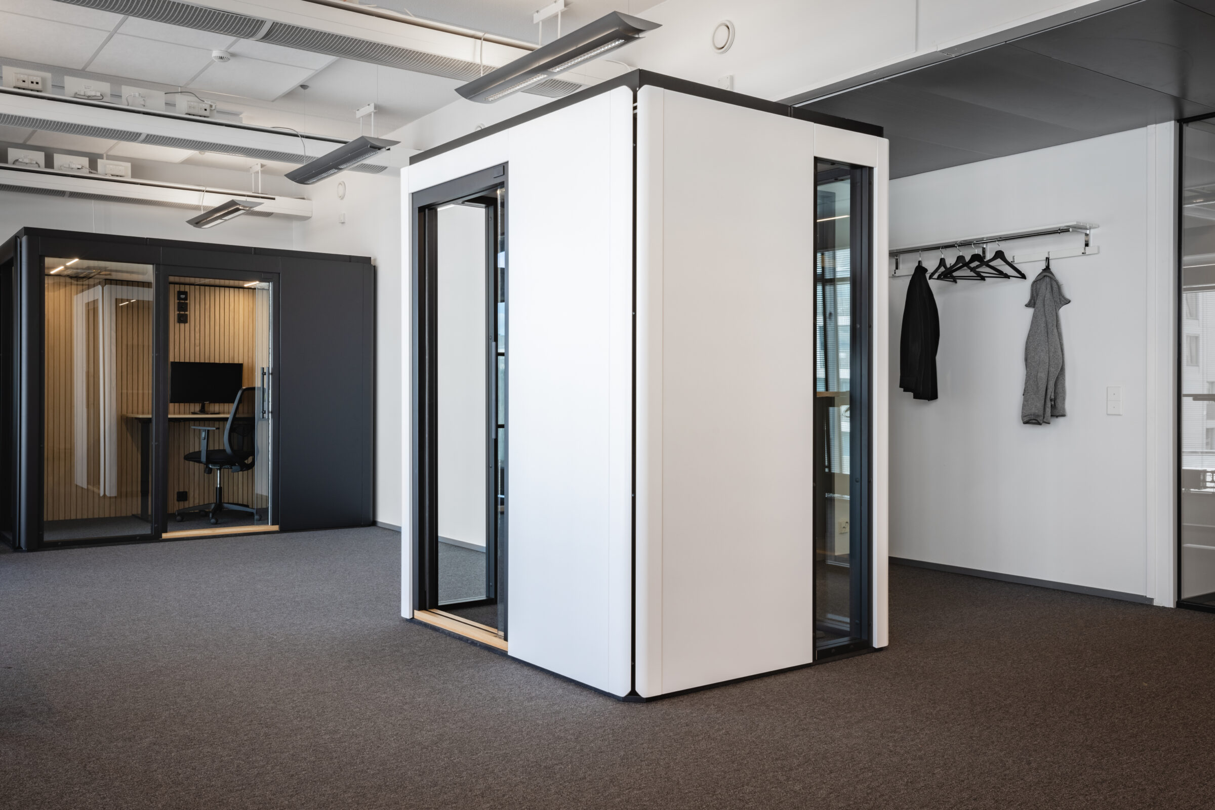Modular office workrooms inside the Huudi office showroom in Helsinki, featuring white and black soundproof pods in an open workspace.