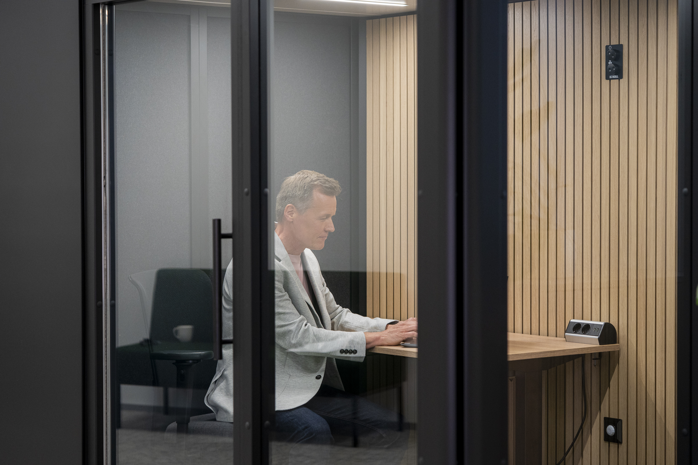 henkilö työskentelee keskittyneesti äänieristetyn työtilan sisällä