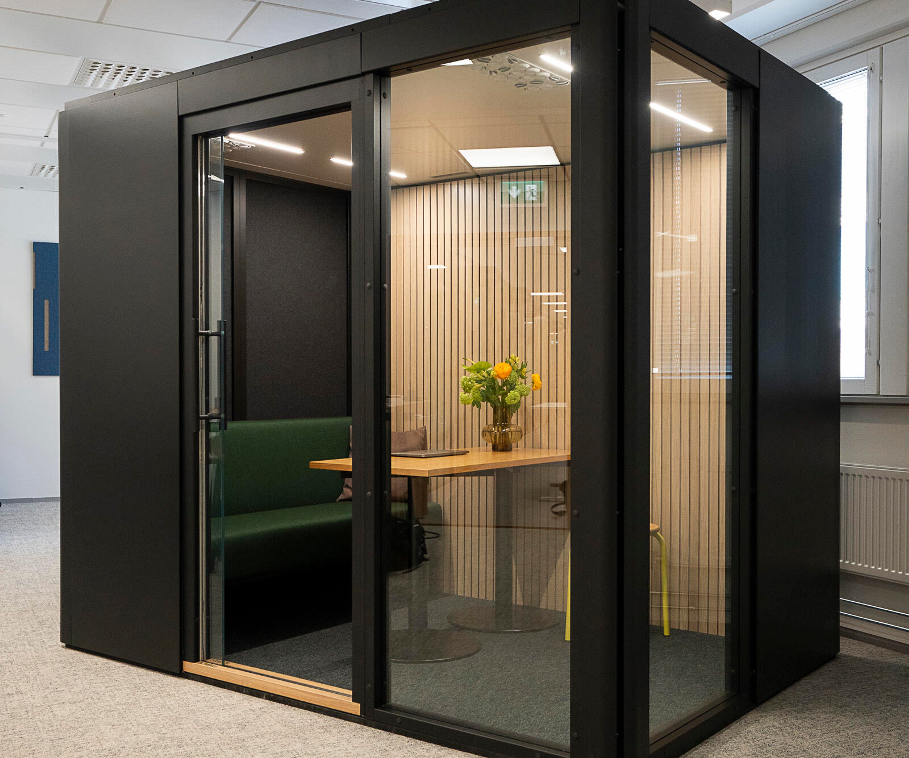 An Octacell workroom with black surfaces and glass wall panels placed in an office space